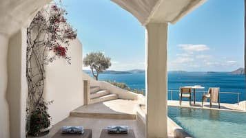A poolside area with two lounge chairs, a small table, and a view of the sea.