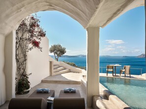 A poolside area with two lounge chairs, a small table, and a view of the sea. - Andronis Boutique Hotel (Santorini)