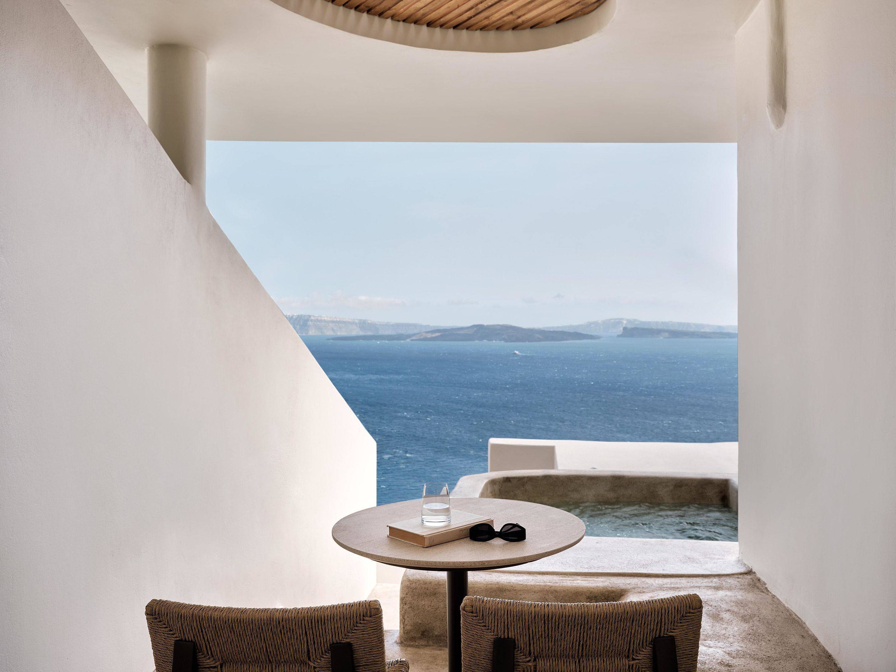 Een balkon met uitzicht op zee, een ronde tafel met een boek en zonnebril, en rieten stoelen.