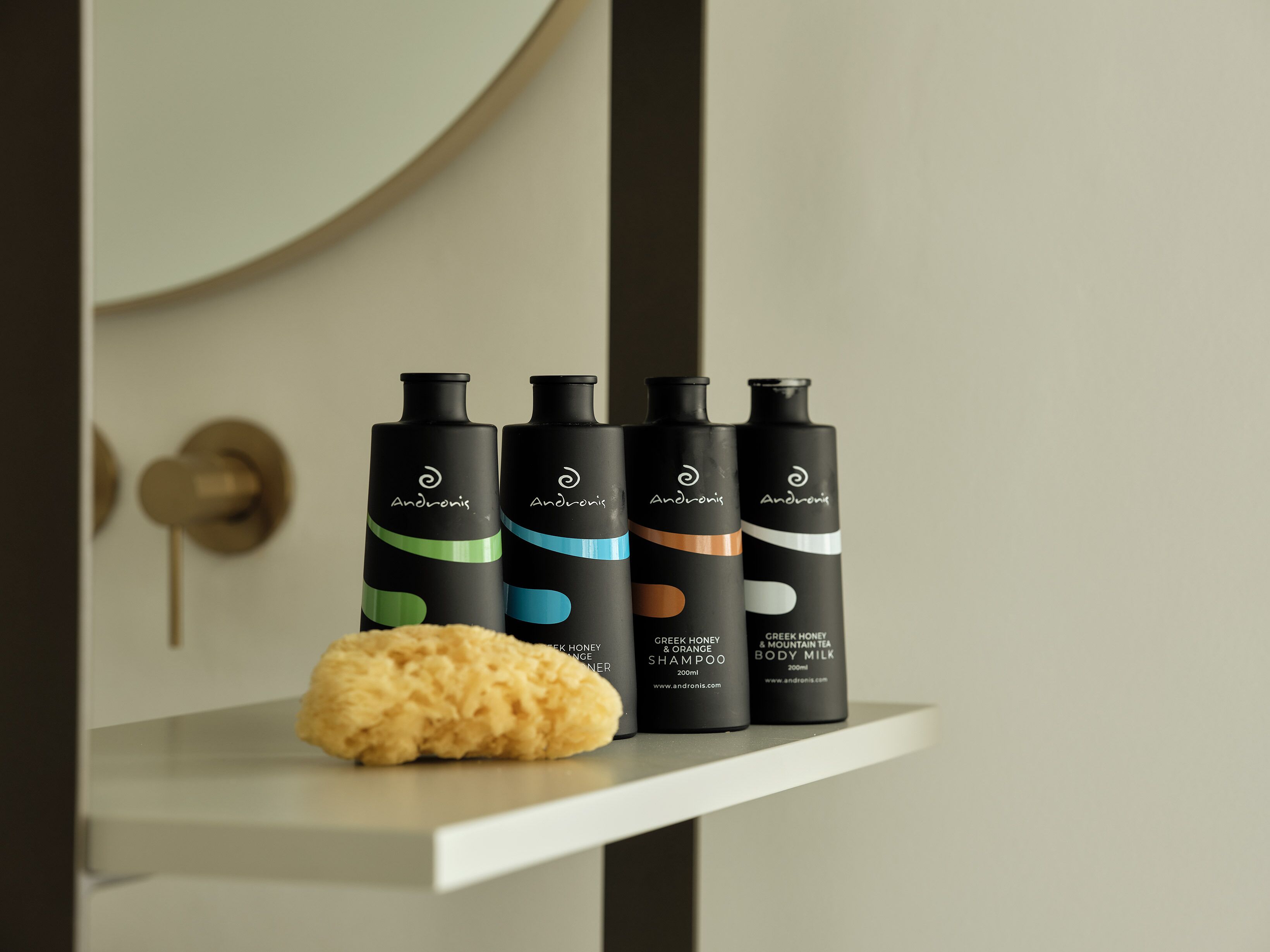 Four bottles of Andronicis body care products on a white shelf.