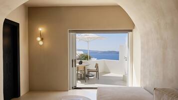 A modern room with a sofa, a small table with a book, and a view of a balcony with a table and chairs.