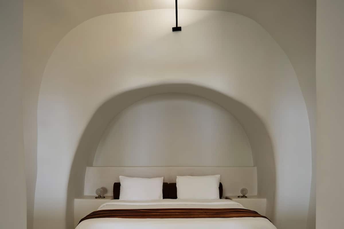 A minimalist bedroom with a curved ceiling, a bed with white bedding, and two bedside tables with lamps.