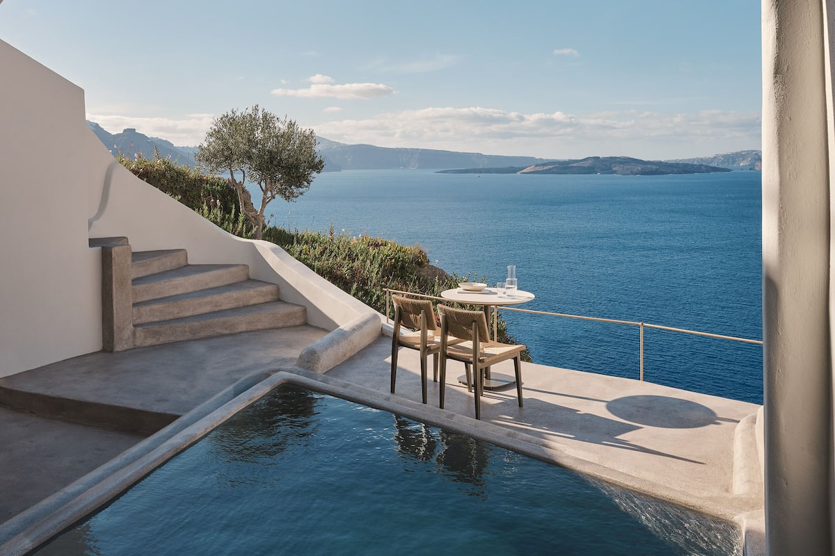 A modern outdoor pool area with a view of the sea, a table with chairs, and a staircase leading to a higher level.