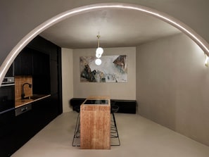 A modern kitchen with a curved ceiling, a central island, and a painting on the wall.