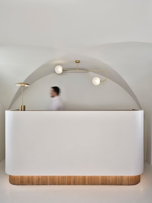 A modern reception desk with a minimalist design, featuring a curved arch and a wooden base.
