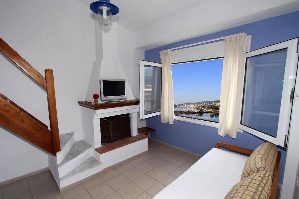 A bedroom with a bed, a TV on a stand, a fireplace, and a window with a view.