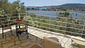 A terrace with stone flooring, a table with chairs, and a view of a lake and hills. - Villa Ariadni (Skiathos)