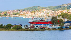 A coastal town with a large red and white ship docked at the harbor, surrounded by smaller boats and buildings. - Villa Ariadni (Skiathos)