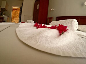 A neatly made bed with white linens and red flowers, a wooden headboard, and a red wall. - Villa Ariadni (Skiathos)