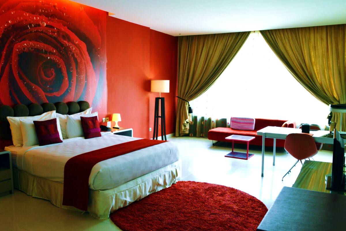 Een moderne hotelkamer met een groot bed, een rood tapijt, een bureau en uitzicht op het omliggende landschap.
