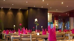 Un restaurante con varias mesas, cada una con servilletas rosas y un florero con una flor blanca.