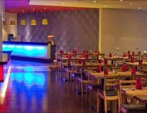 Un restaurante con diseño moderno, que destaca por una barra central y varias mesas con servilletas rojas.