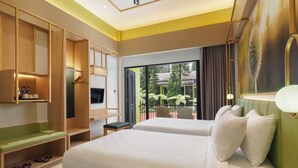 Habitación de hotel con cama, televisor, zona de estar y balcón con vistas a zonas verdes.