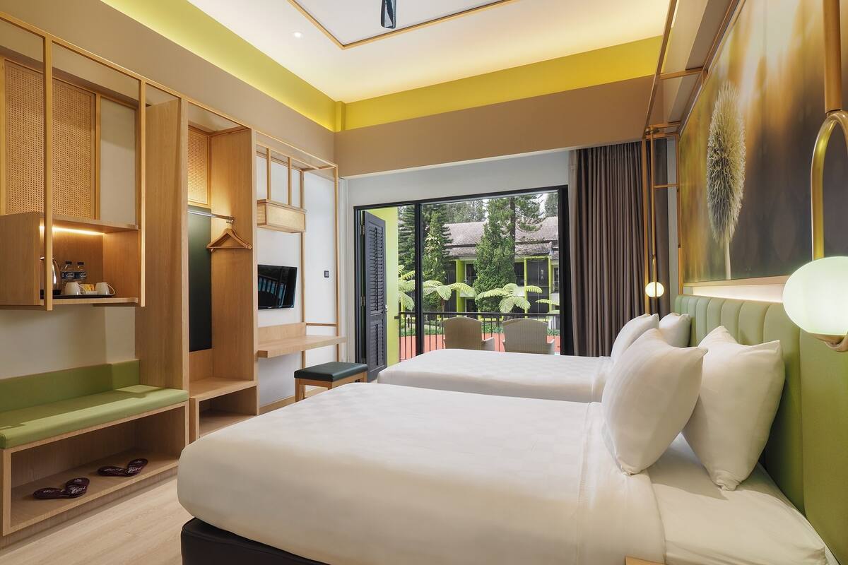 Hotelkamer met een bed, een televisie, een zithoek en een balkon met uitzicht op groen.