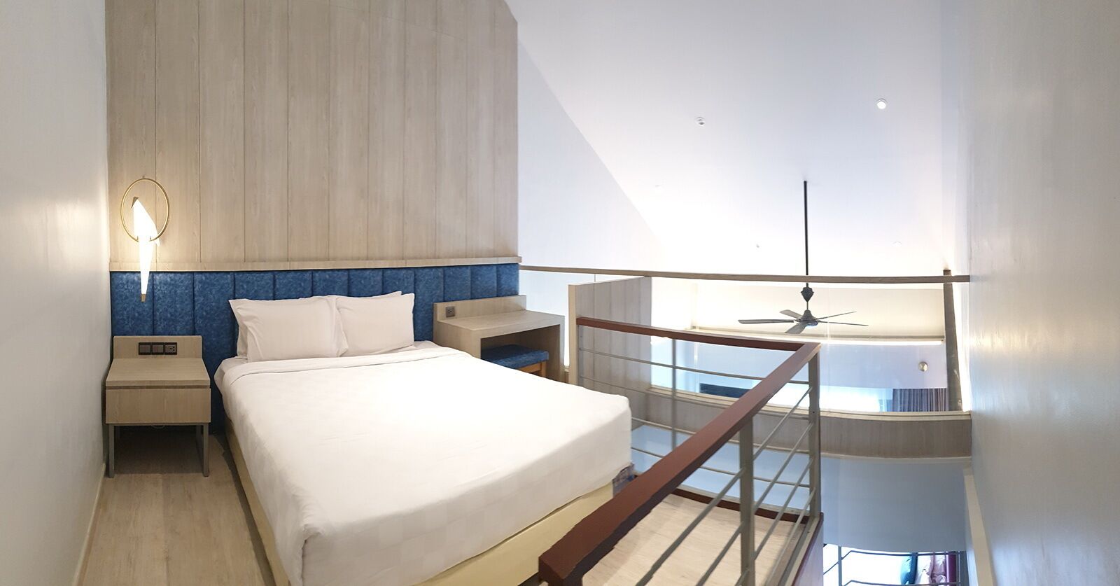 A modern hotel room with a large bed, a nightstand, a desk, and a balcony with a ceiling fan.