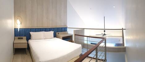 A modern hotel room with a large bed, a nightstand, a desk, and a balcony with a ceiling fan.