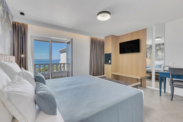 A modern hotel room with a large bed, a desk, a TV, and a balcony with a view.