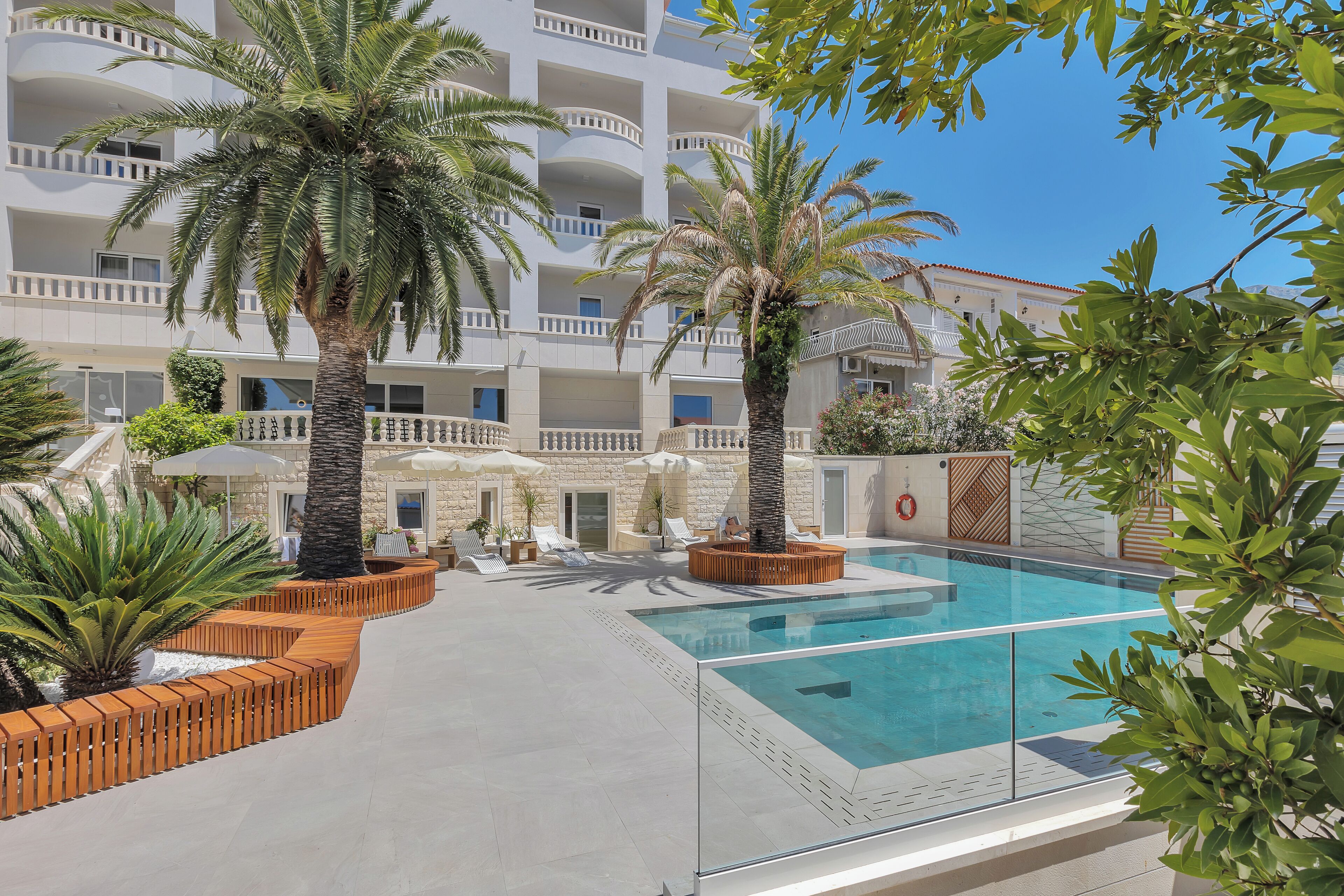 A pool area with palm trees, lounge chairs, and a building with multiple balconies.