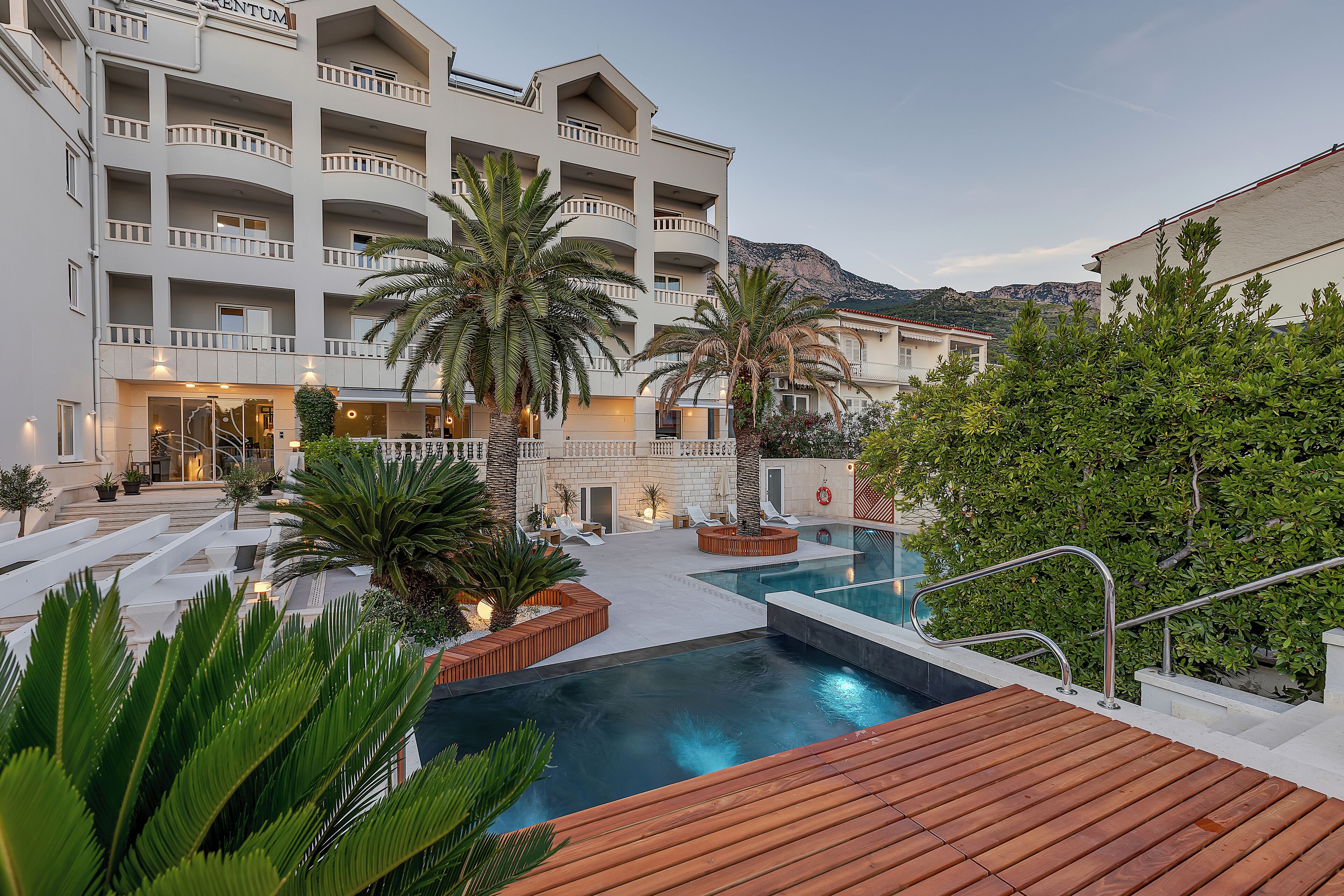 A hotel with multiple balconies, a swimming pool, and a mountainous backdrop.