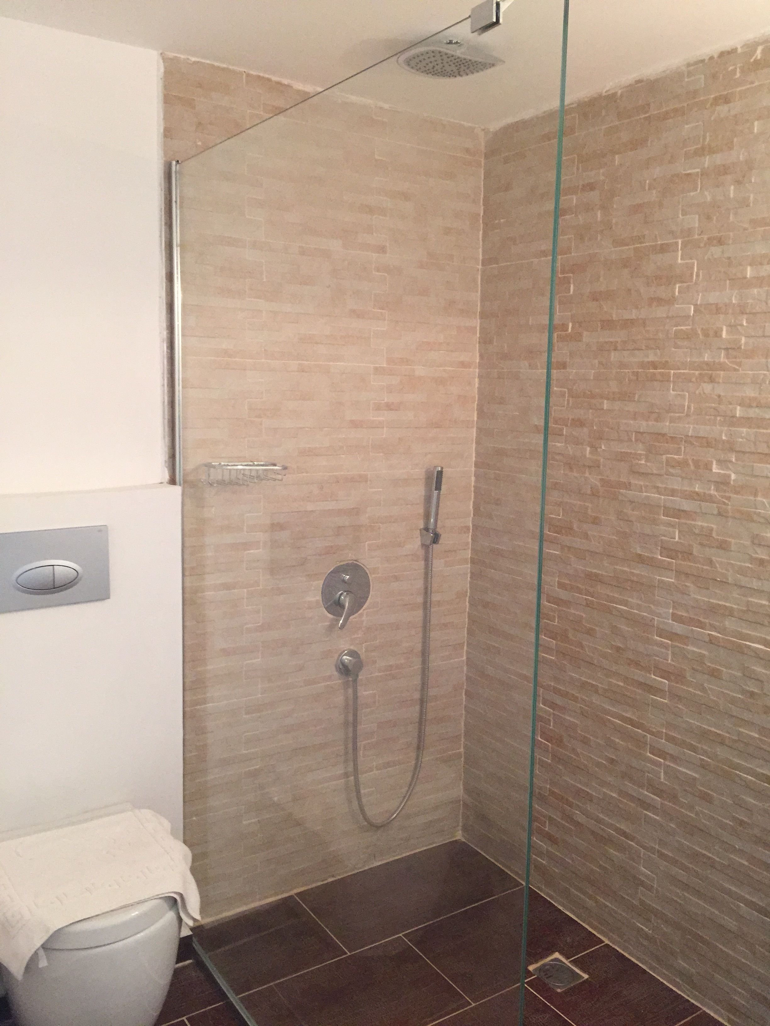 A shower area with a glass door, a toilet, and a wall-mounted control panel.