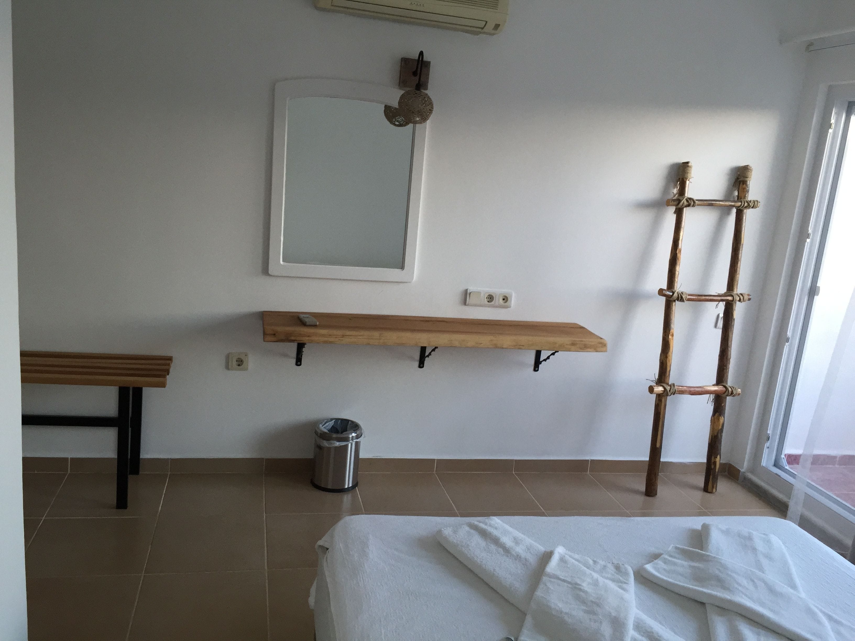 Een kamer met een bed, een houten plank, een spiegel, een wandheater, een prullenbak en een houten trap.