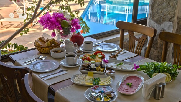 A table set for breakfast with various dishes, a vase of flowers, and a view of a swimming pool. - Hotel Pataros (Kas)