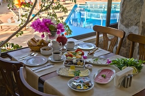 Taula preparada per esmorzar amb diversos plats, un ram de flors i vista a una piscina.