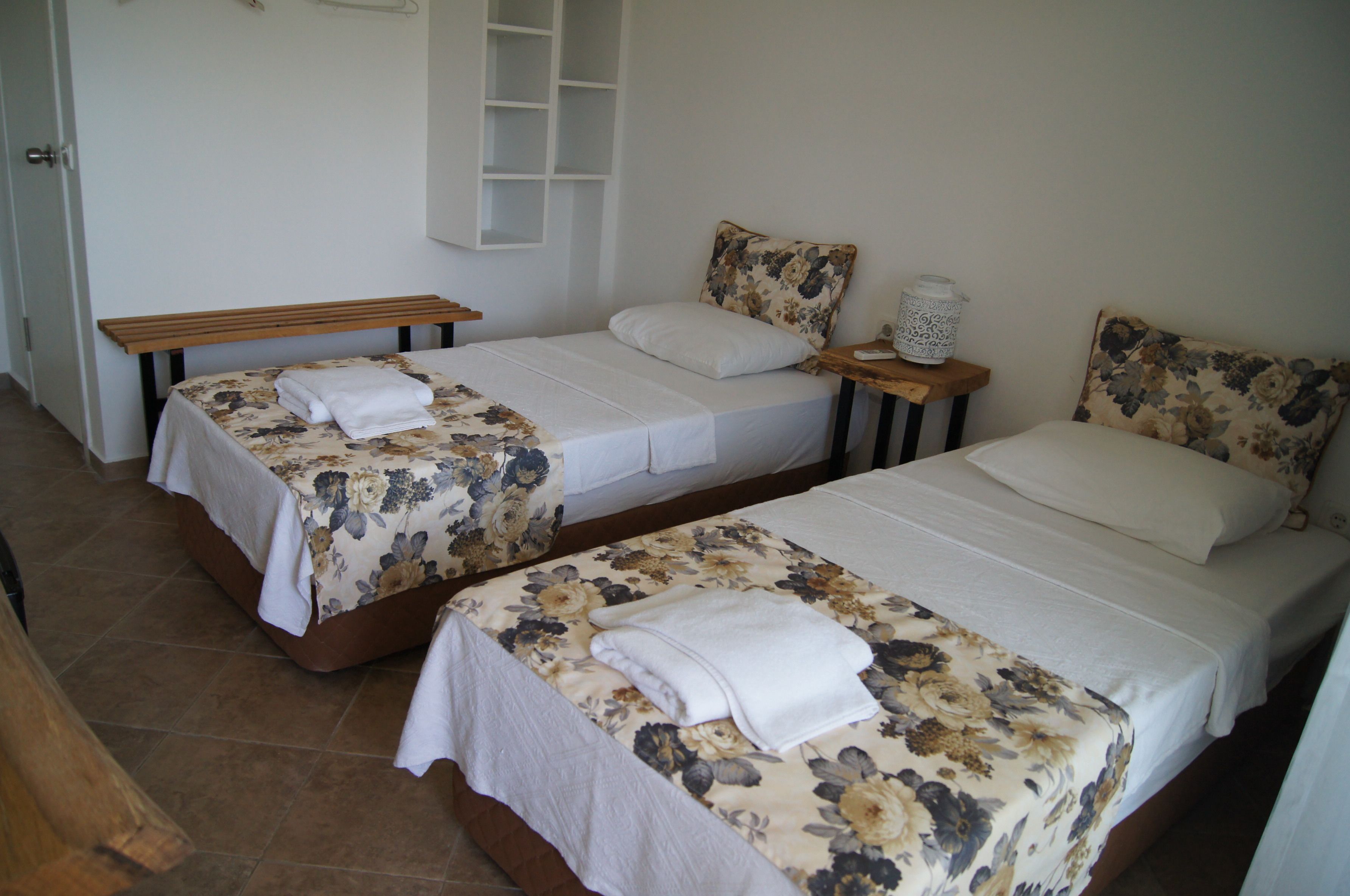Two single beds with floral bedding, a wooden bench, and a bedside table with a lamp.