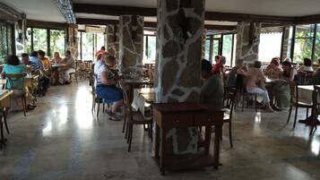 A spacious dining area with stone pillars, wooden tables, and chairs.