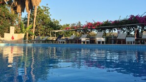 A swimming pool with lounge chairs and a pergola with pink flowers. - Hotel Pataros (Kas)