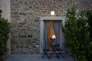 A stone building with a door leading to a room. There is a table and chairs outside the door. - La Cianella (Scarlino)