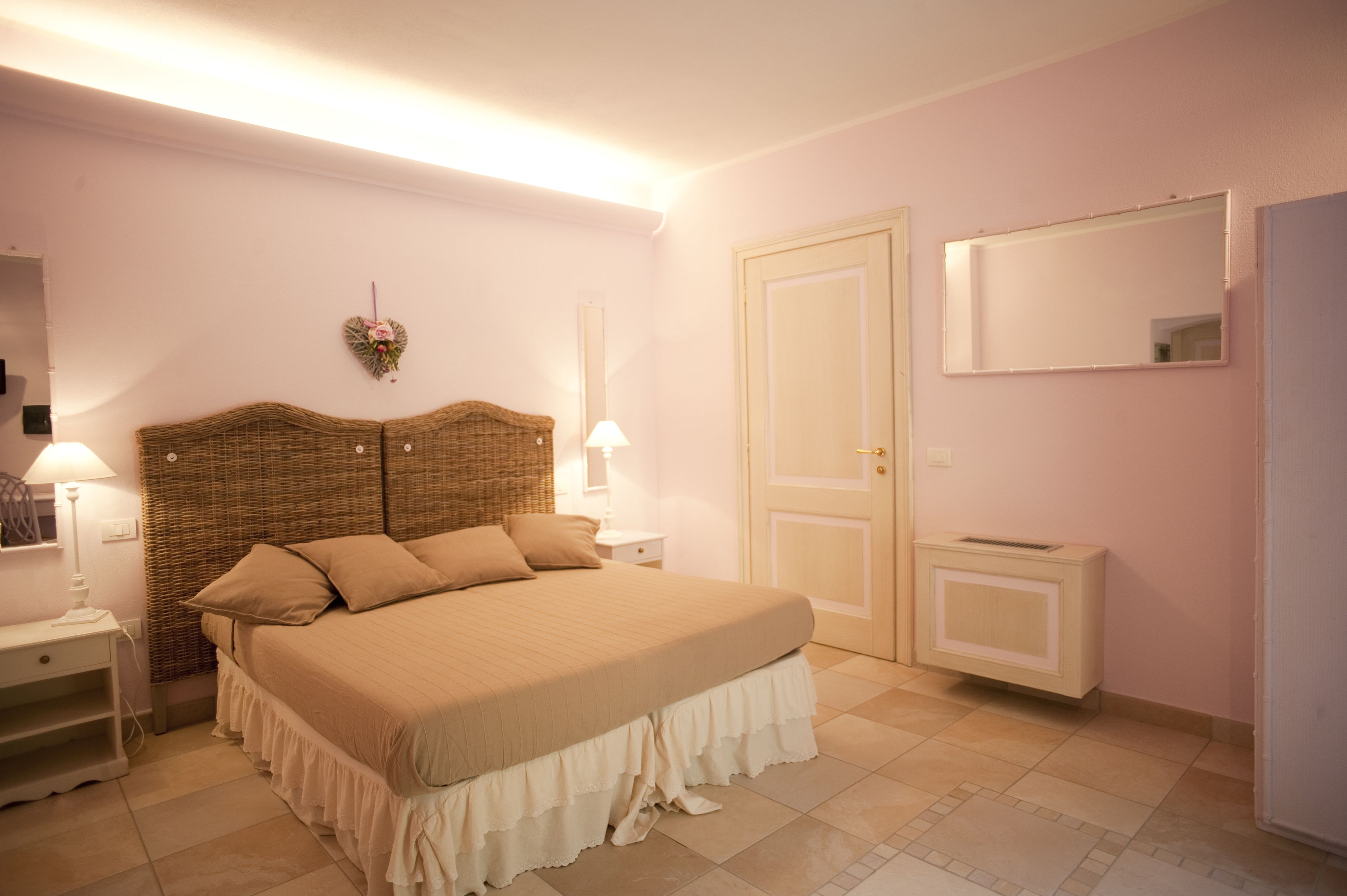 Una camera da letto con un letto grande, un comodino con una lampada, una cassettiera, uno specchio e una porta.
