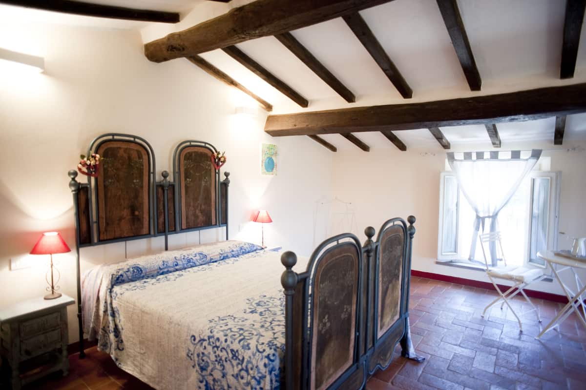 A bedroom with a wooden bed frame, a bedside table with a lamp, and a window with curtains.