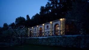 Un edificio de paredes de piedra con ventanas arqueadas y barandilla metálica, rodeado de árboles.
