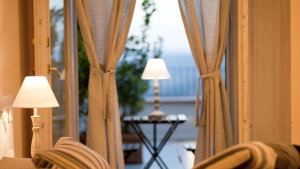 Una habitación de hotel con una cama, dos lámparas de noche y vistas al exterior a través de cortinas.