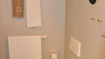 Un baño con inodoro, bidé, toallero, radiador y una lámpara de pared.