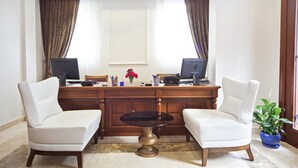 Un entorno de oficina profesional con dos sillas blancas, un escritorio de madera, dos monitores y un florero con flores.