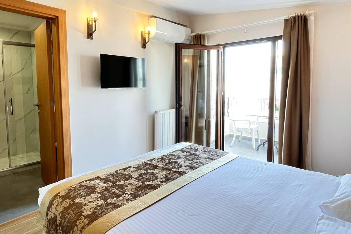 A hotel room with a bed, a TV, a sliding glass door to a balcony, and a shower area.