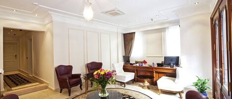 A spacious living room with a round coffee table, leather armchairs, a white sofa, and a desk with a computer.