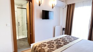 Habitación de hotel con cama, televisor, ducha y ventana con cortinas.