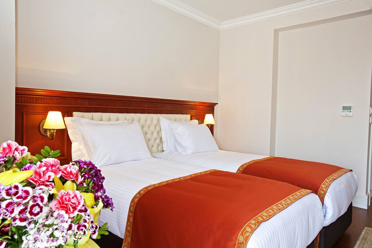 A hotel room with a large bed, two bedside tables, a wooden headboard, and a bouquet of flowers.