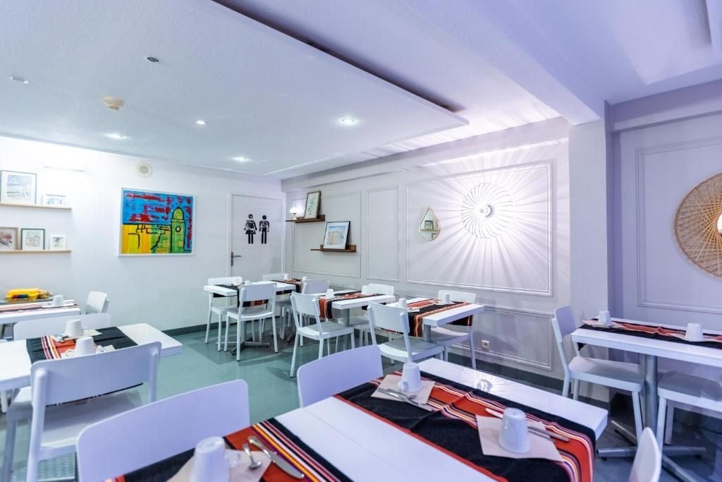 A modern dining area with white tables and chairs, artwork on the walls, and a decorative wall piece.