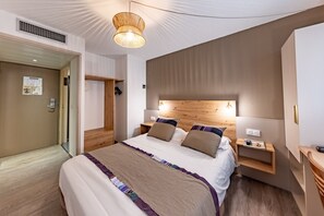 Una habitación de hotel moderna con una cama grande, cabecera de madera, mesitas de noche y una lámpara colgante.
