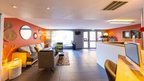 A modern hotel lobby with a sofa, chairs, a reception desk, and decorative wall art.