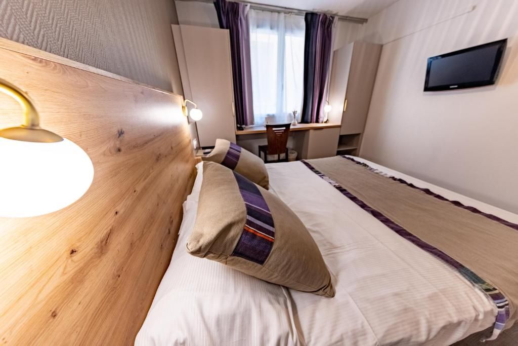 Une chambre d’hôtel avec un lit, un bureau, une chaise, une télévision et une fenêtre avec des rideaux.