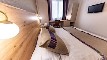 Une chambre d’hôtel avec un lit, un bureau, une chaise, une télévision et une fenêtre avec des rideaux.
