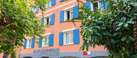 Un hotel de varios pisos con contraventanas azules, fachada de piedra y un letrero que dice 'Princes de Catalogne'.