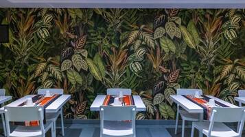 A dining area with tables and chairs, a patterned wall, and a ceiling vent.