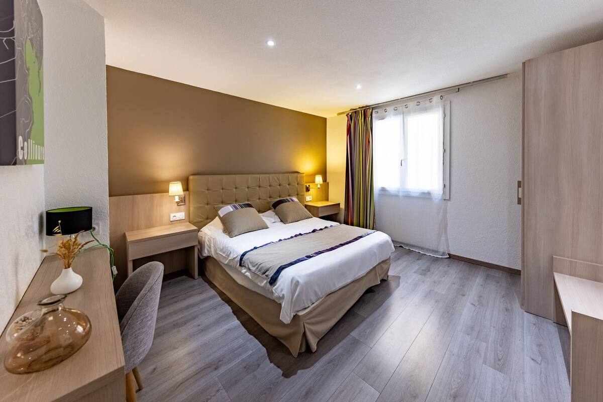 Un dormitorio moderno con una cama grande, mesitas de noche, un escritorio y una silla.