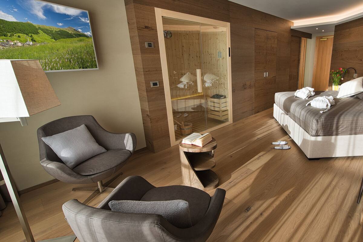 Un dormitorio moderno con una cama grande, un armario de madera, una zona de estar con sillas y suelo de madera.
